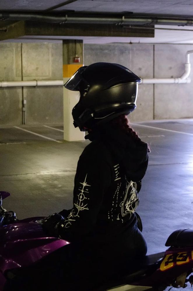 Rider in a black helmet seen in profile on a purple motorcycle, the COMMIT hoodie sleeve design and back print in view